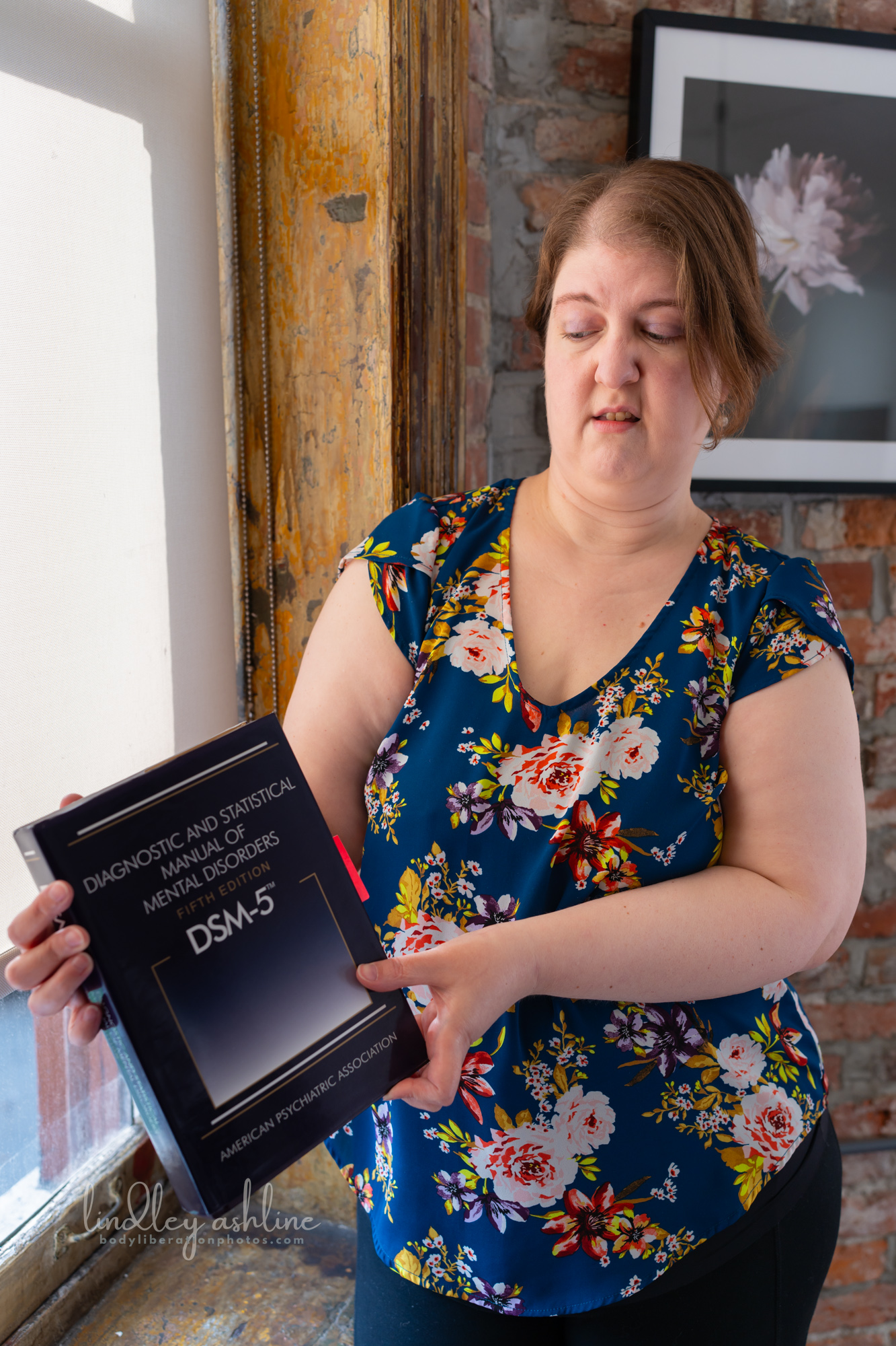 A chronically ill therapist makes a face at a copy of the DSM-5 book at a Pacific Northwest fat-positive business branding photo shoot.