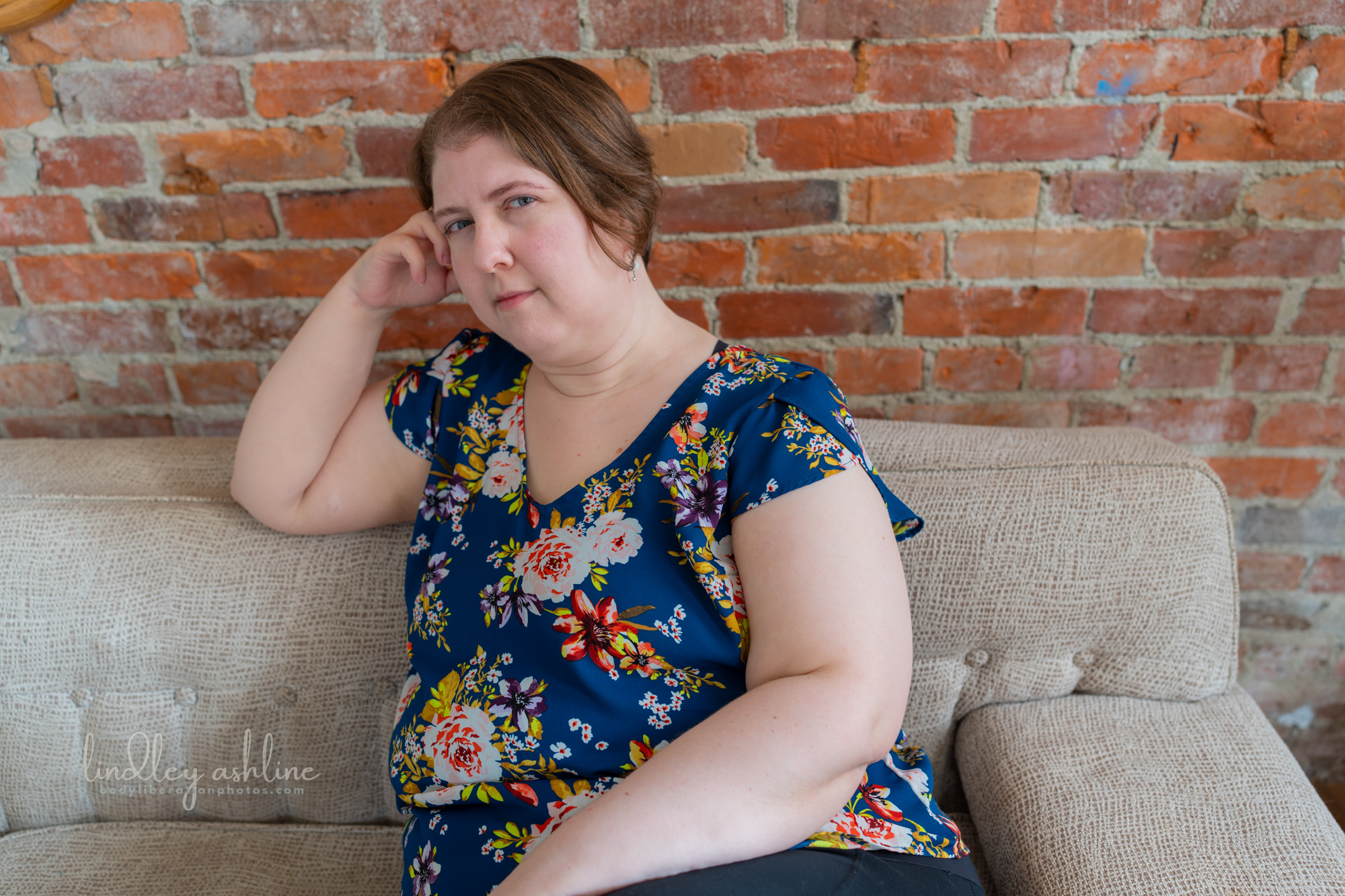 A plus-size white woman in a sleeveless top rests on a couch at a Seattle fat-positive business branding photo shoot.
