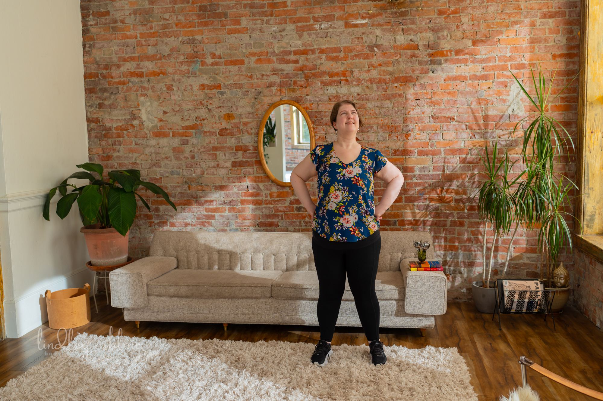 A plus-size white woman in a sleeveless top stands in front of a couch at a Seattle fat-positive professional portrait photo session.